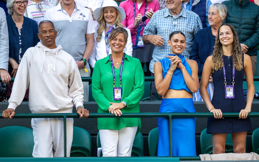 a man and three women stand and smile behind a green fence