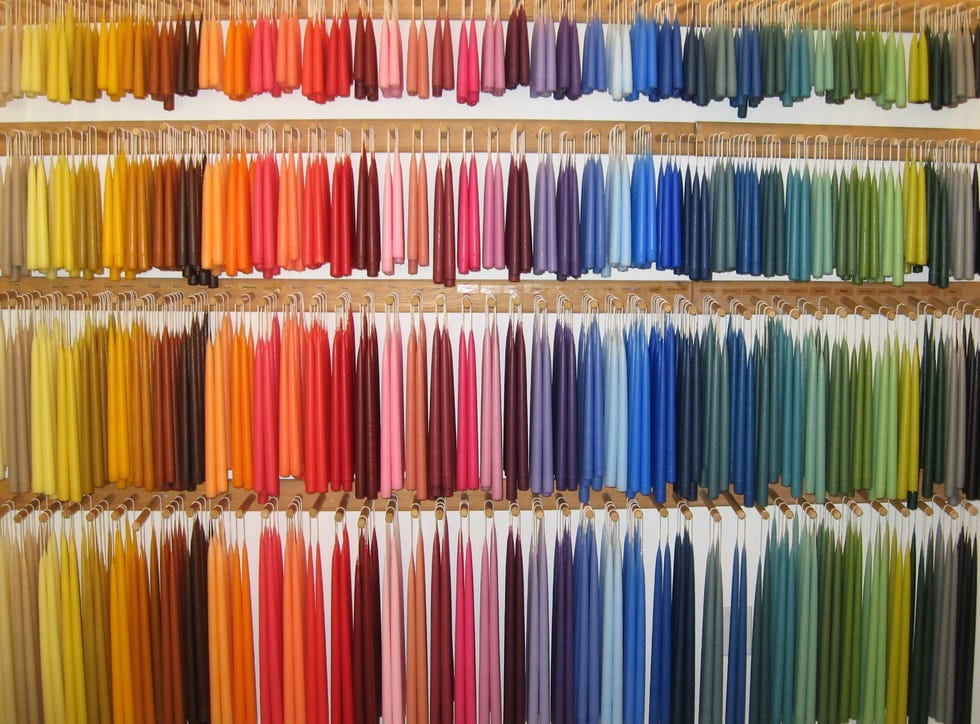 Display of various colorful taper candles organized in rows.