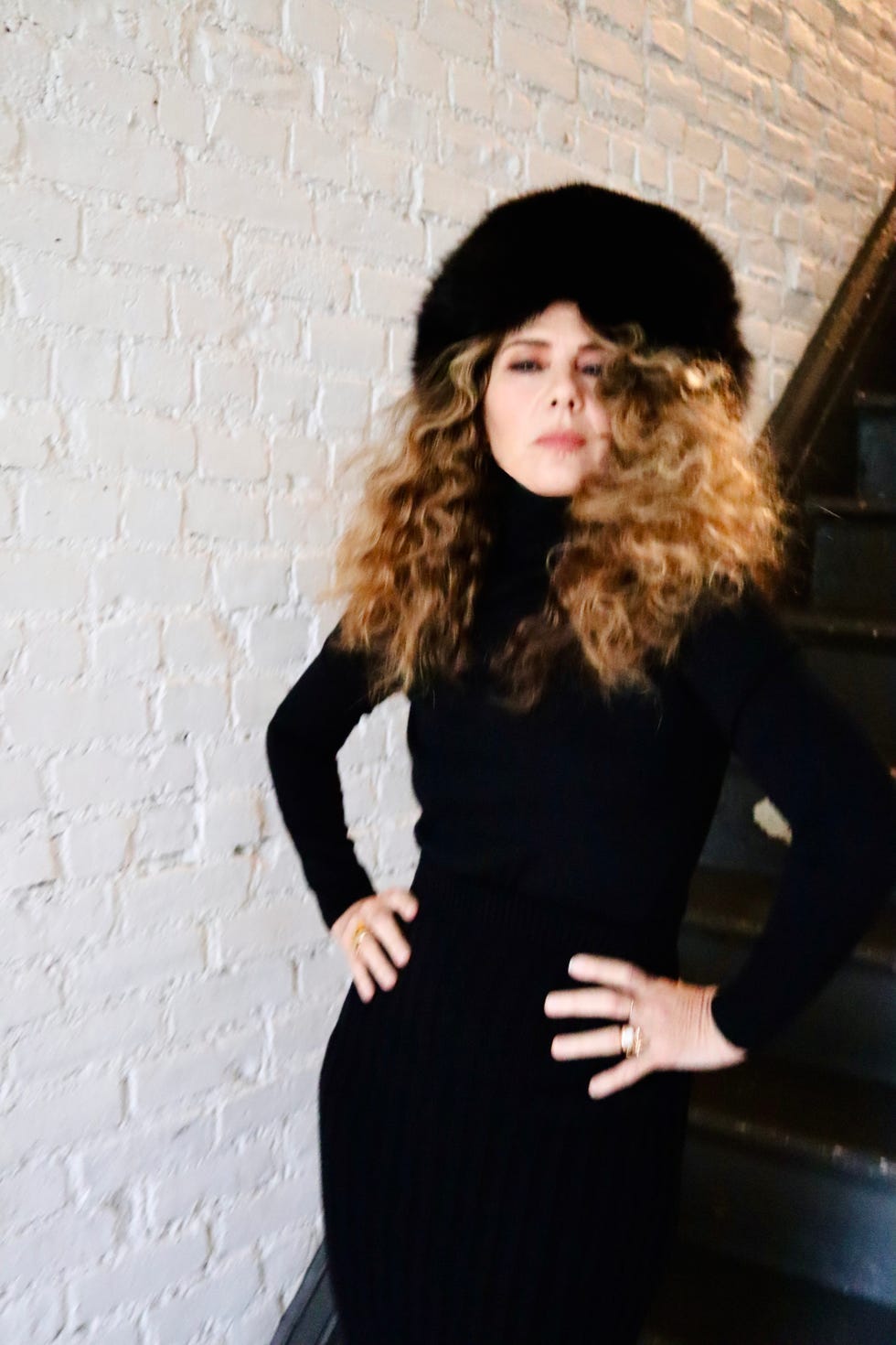 woman posing confidently in a black outfit against a brick wall