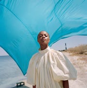 model stands on beach in white dress in front of blue tarp model stands on beach in white dress in front of blue tarp