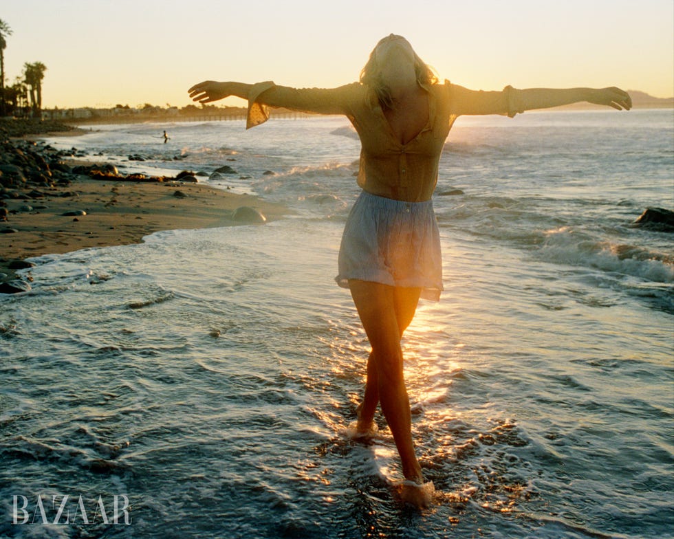 colored image of anna ewers near shore posing with arms out