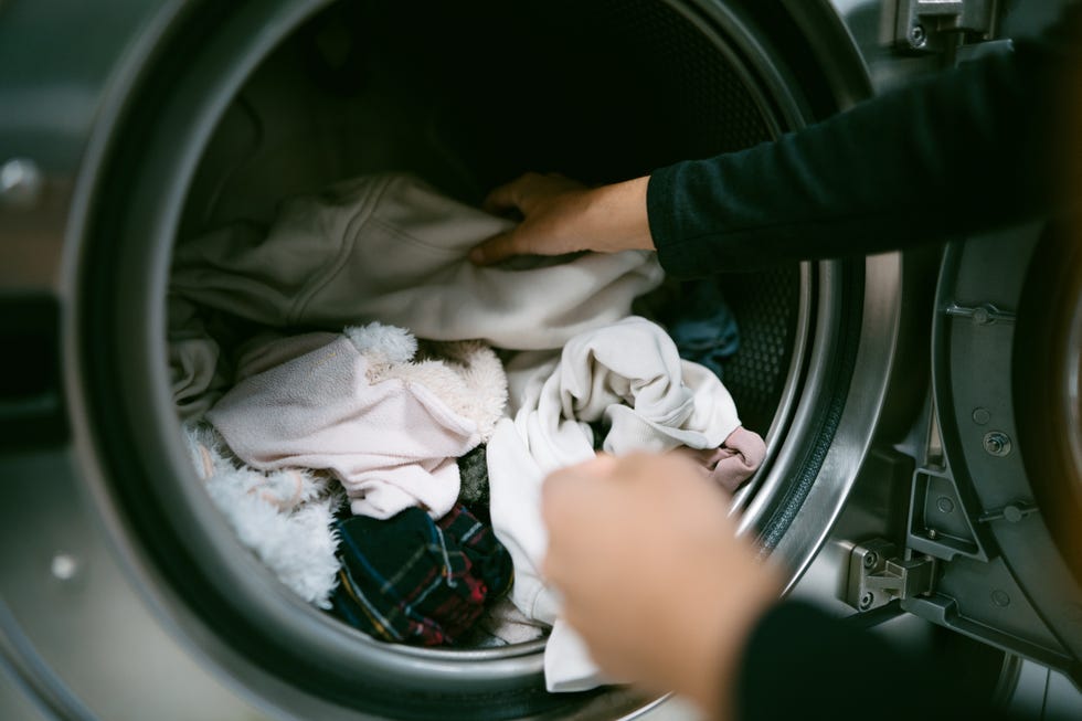 young caucasian woman hands putting her dirty clothes in the washing machine in a laundromat. self service laundry