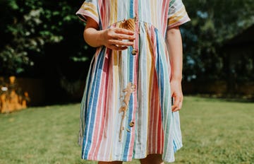 comical and relatable image of a young girl in a domestic garden. she drips melted ice cream all down the front of her stripy linen dress. depicts summer and stains.