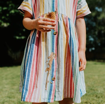 A little girl drips chocolate / vanilla ice cream all over her nice linen dress on a hot summers day comical and relatable image of a young girl in a domestic garden. she drips melted ice cream all down the front of her stripy linen dress. depicts summer and stains.
