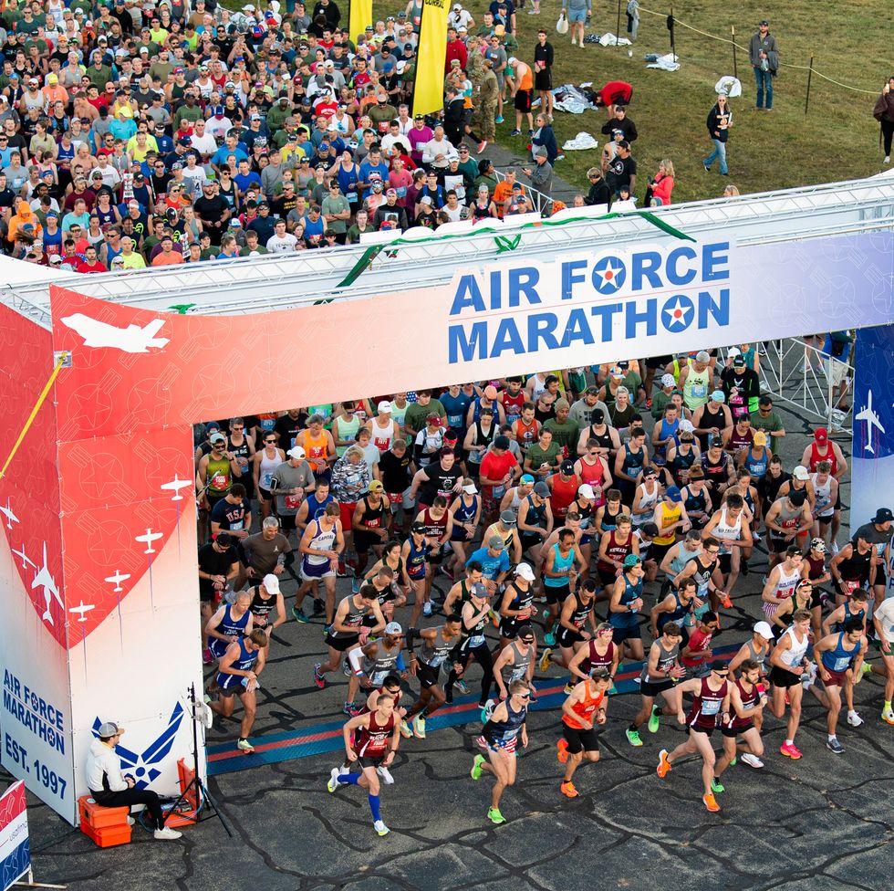 a crowd of runners at the start of a race pass under a sign reading air force marathon
