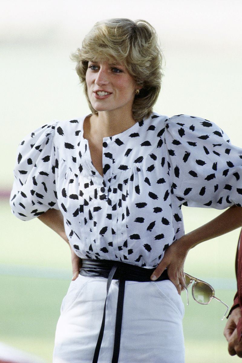 Princess Diana at the polo wearing a paintbrush print white blouse with puffy sleeves, a white skirt and a cinched wrap-around black leather belt