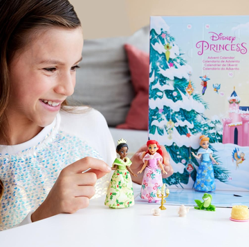 disney princess advent calendar 2024 a child is interacting with an advent calendar themed around disney princesses the calendar features a colorful backdrop of a castle and a winter scene several small collectible figures of princesses including characters in colorful dresses are placed on a white table alongside the figures are various small accessories and toys such as a frog a cake and other themed items related to the series the scene conveys a festive and playful spirit