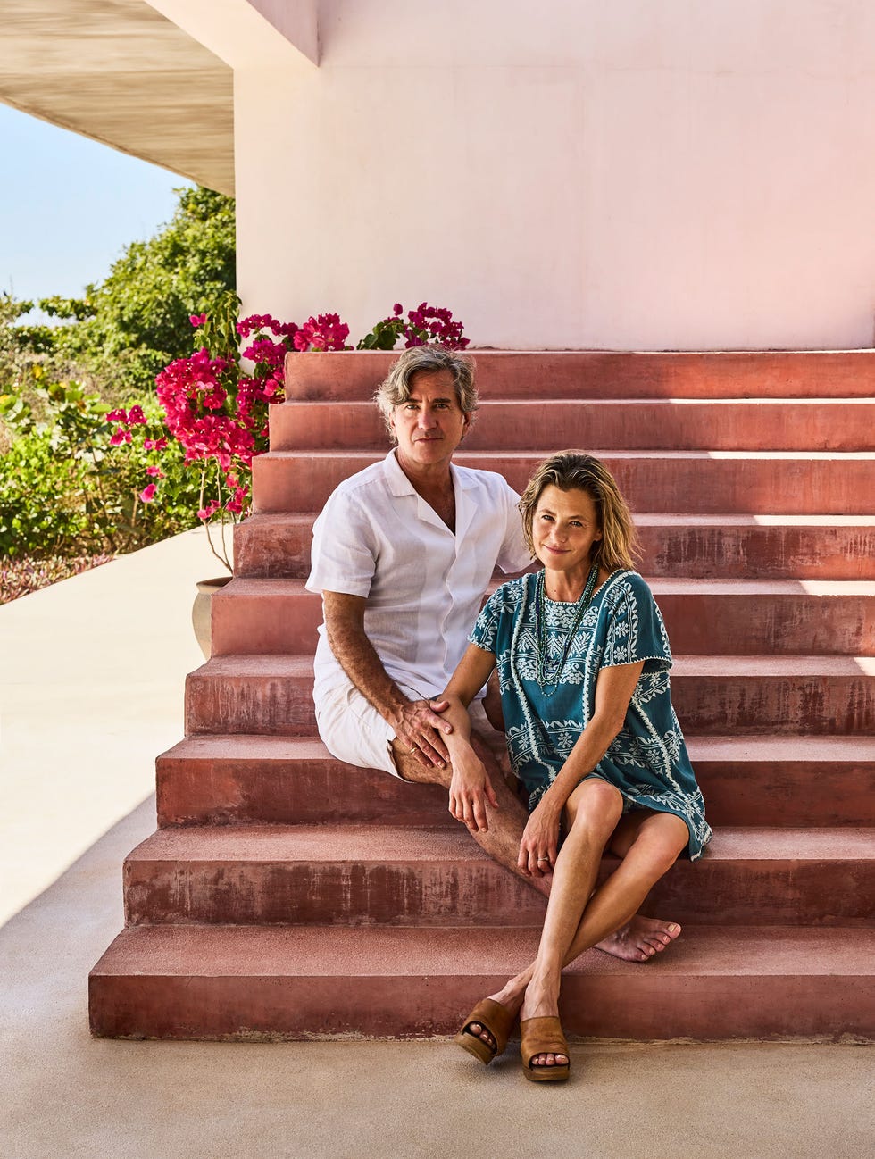 A couple seated on steps with vibrant flowers in the background.