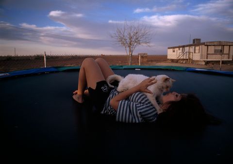 Onder dreigende wolken in Mentone Texas relaxt een jonge vrouw met haar kat op een trampoline