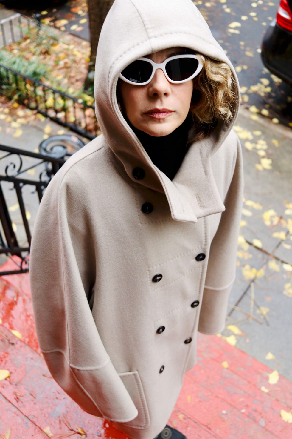 a person wearing a beige coat with a hood stands on red steps