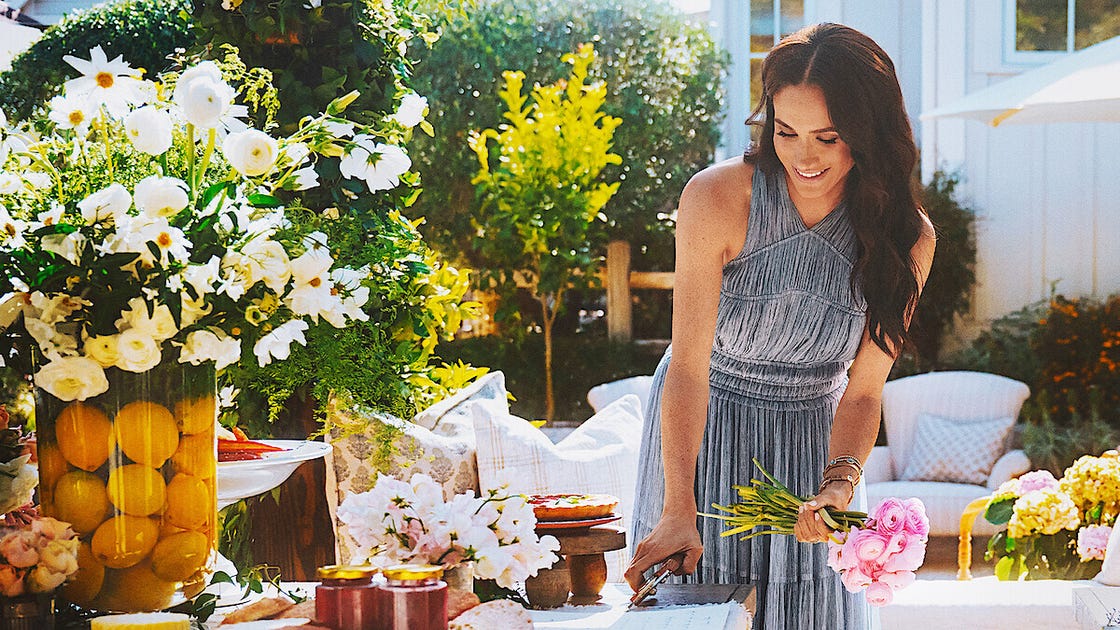 A woman arranging flowers at a festive outdoor table adorned with decorations and food.