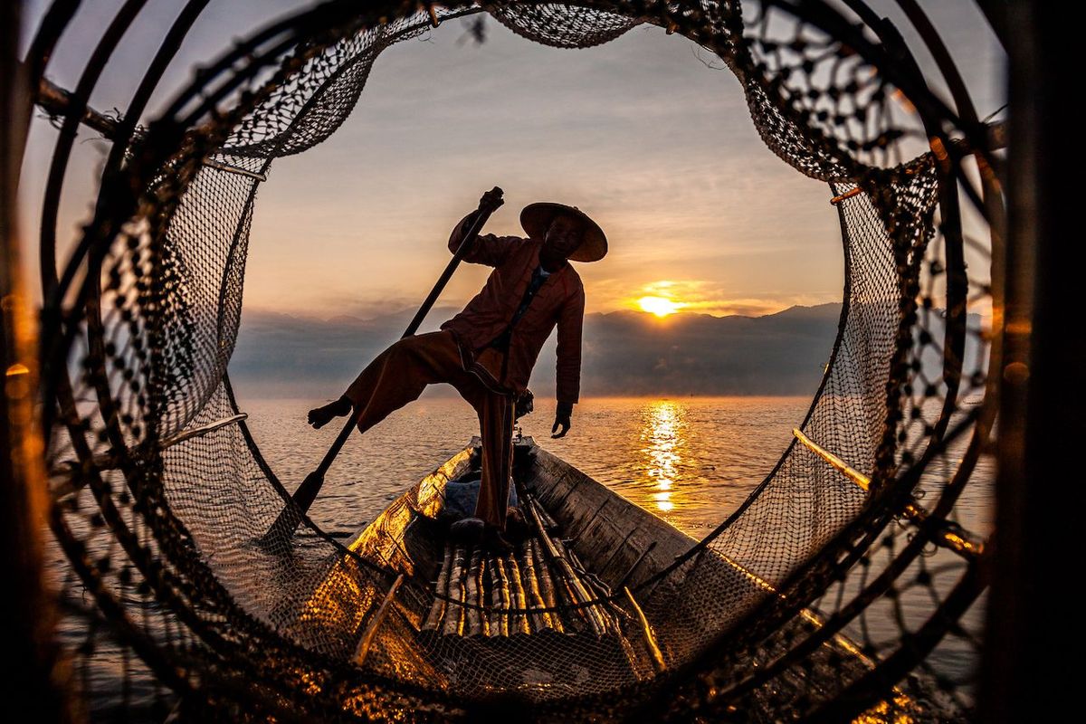 Publiekswinnaars Mens In de vroege ochtend met een bootje het Inlemeer op Tijdens de zonsopgang vist het Intha volk nog op traditionele wijze De afbeelding laat de ongelofelijke balans zien die deze mensen hebben