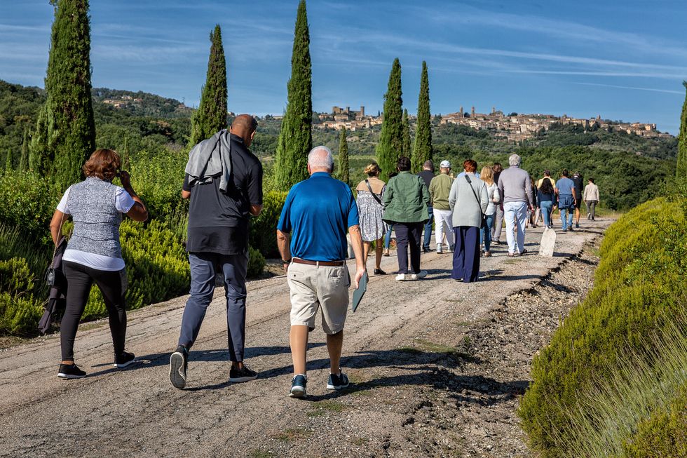 A group of people walk by a vineyard in Tuscany.