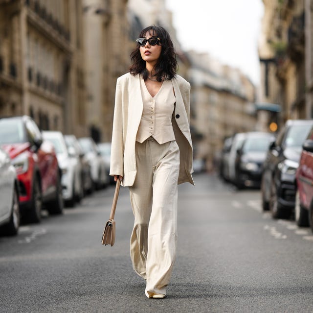 woman walking in a linen three piece suit holding a linen colored mini handbag wearing black sunglasses