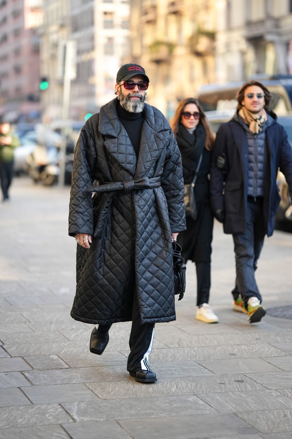 milan, italy january 13 a guest wears a cap, sunglasses, a black pullover, a black long padded puffer trench coat, sportswear pants, black shoes, outside msgm, during the milan fashion week menswear fallwinter 2024 2025 on january 13, 2024 in milan, italy photo by edward berthelotgetty images