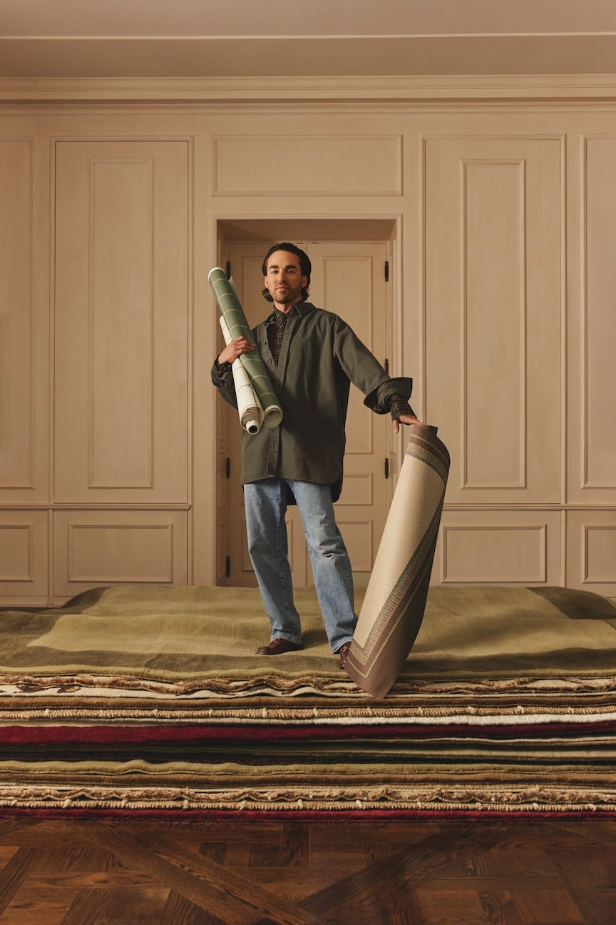 person holding rolls of carpet and a rug in a room with wooden flooring