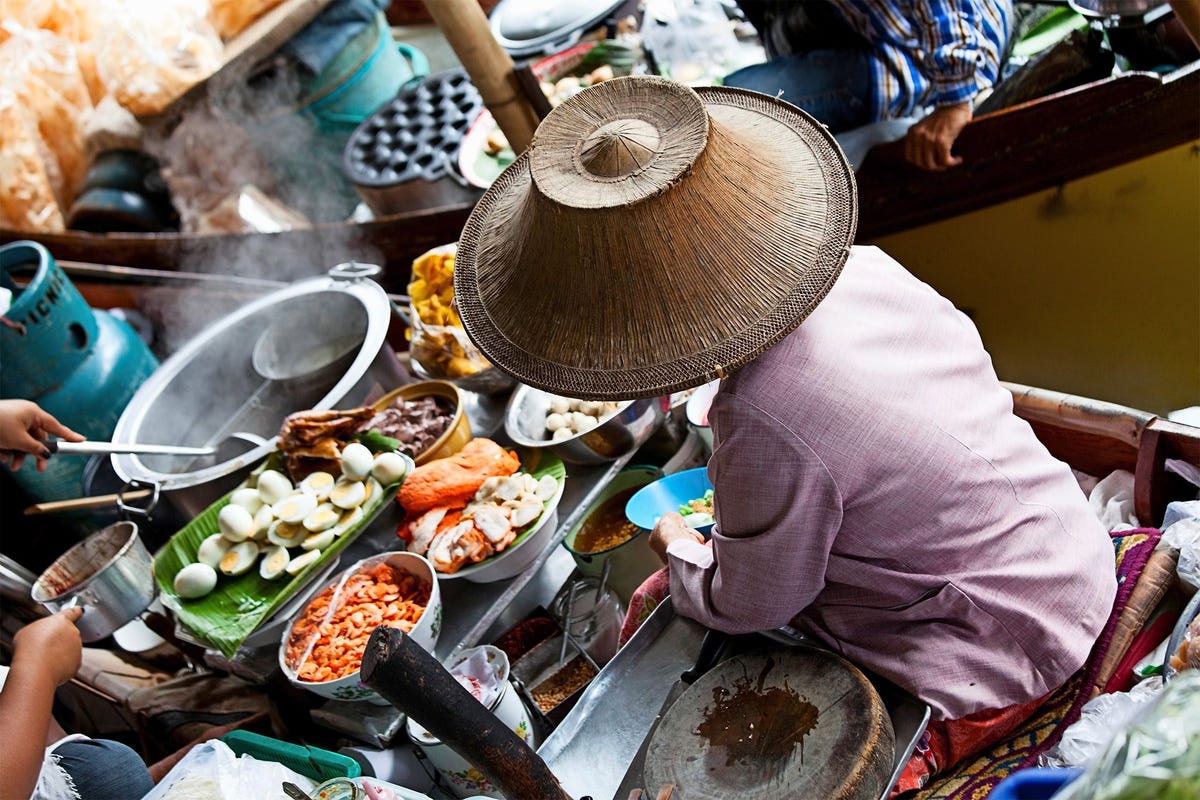 Op de drijvende markt van Damnoen Saduak verkoopt een vrouw traditionele Thaise gerechten vanuit haar boot