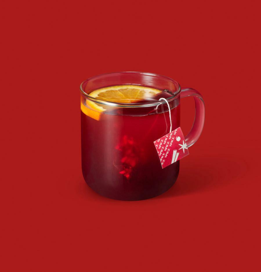 a clear glass mug filled with red beverage topped with a slice of orange and a tea bag