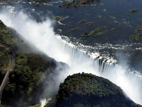 VANUIT DE LUCHT  De grens tussen Zimbabwe en Zambia verloopt door het midden van de rivier de Zambezi en ook het midden van de Victoriawatervallen Op de naburige klippen wordt een regenwoudachtig ecosysteem in stand gehouden door de nevel die de watervallen opwerpen