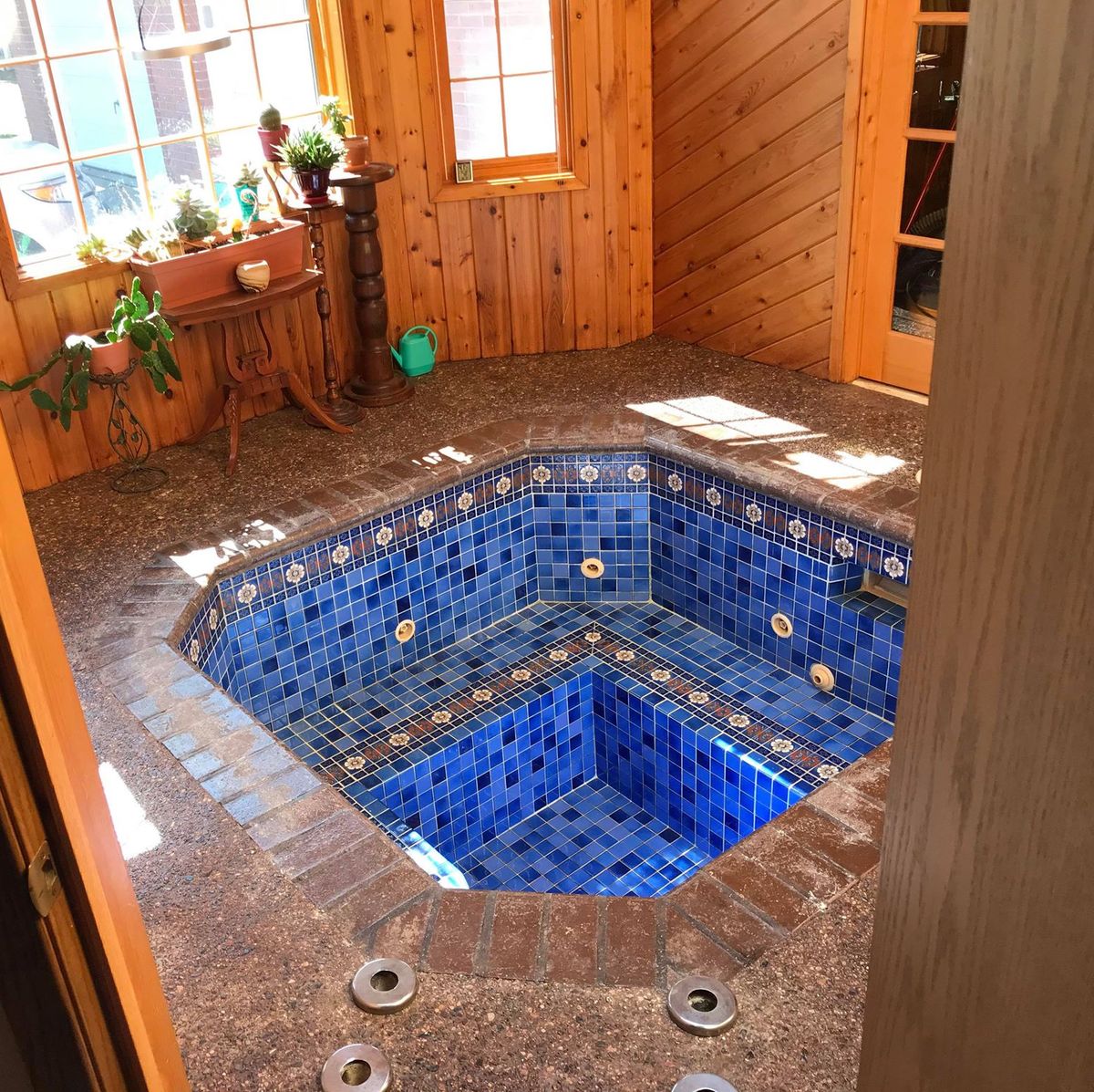 Blue-tiled hot tub inside sunlit room with wood-paneled walls