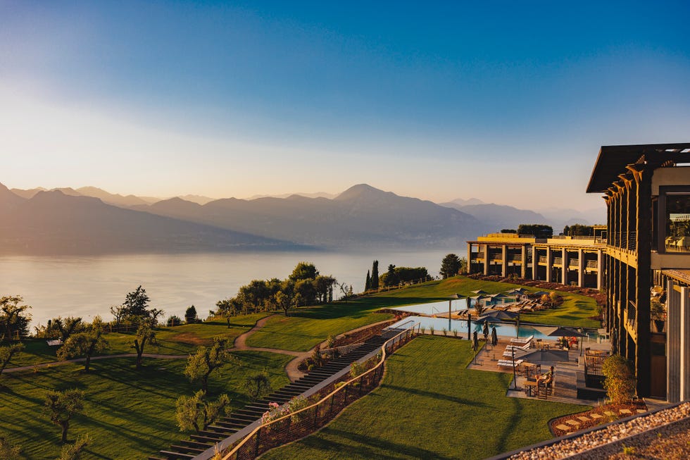 a building with a pool in the front and a large green field with mountains in the background