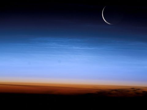 Deze opname werd in 2003 gemaakt door een astronaut aan boord van het International Space Station toen het ruimtestation zich boven Mongoli bevond Een flinterdunne maansikkel is te zien boven een dwarsdoorsnede van de aardatmosfeer waaronder de zelden waargenomen lichtende nachtwolken boven ijle wolkenflarden die op een hoogte van 80 tot 95 kilometer boven het aardoppervlak drijven