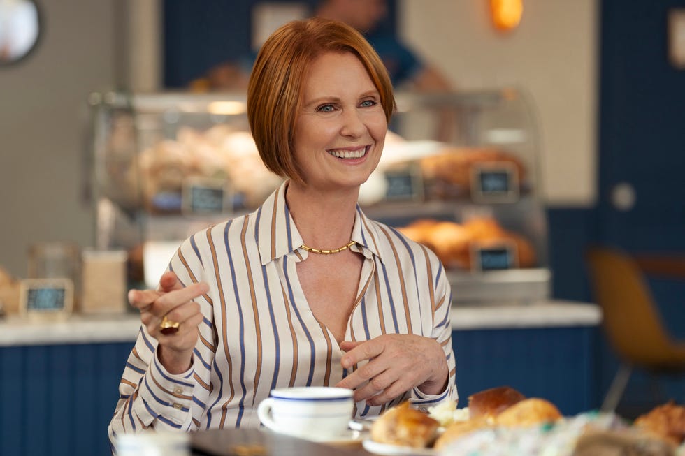 A person gesturing while seated at a table with pastries and a cup.