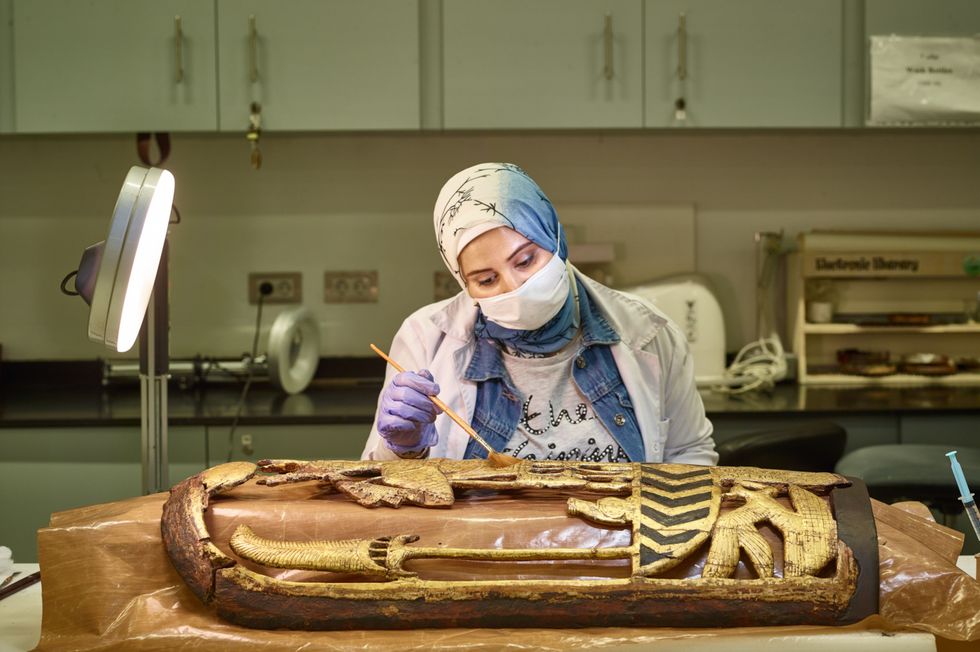 Een medewerker van het Grand Egyptian Museum werkt aan het restaureren van een verguld houten oorlogsschild een van de schatten van Toetanchamon