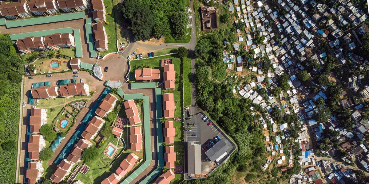 Op een steile rotswand langs de rivier de Umgeni in Durban een stad aan de oostkust van ZuidAfrika is een dure woonwijk verrezen Vanuit hun appartementenflats kijken de bewoners uit over het voetbalstadion Moses Madiba de Durban Country Club en honderden sloppen die op de hellingen zijn gebouwd