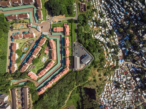 Op een steile rotswand langs de rivier de Umgeni in Durban een stad aan de oostkust van ZuidAfrika is een dure woonwijk verrezen Vanuit hun appartementenflats kijken de bewoners uit over het voetbalstadion Moses Madiba de Durban Country Club en honderden sloppen die op de hellingen zijn gebouwd
