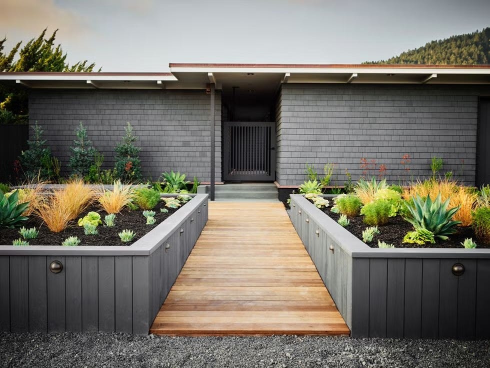 Modern entryway featuring landscaped garden beds and wooden pathway.