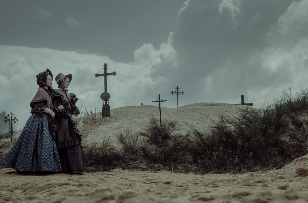 Two women in historical dress standing by a graveyard.