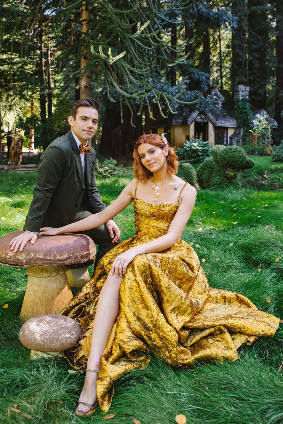 a man and woman sitting on a stump in a yard with trees
