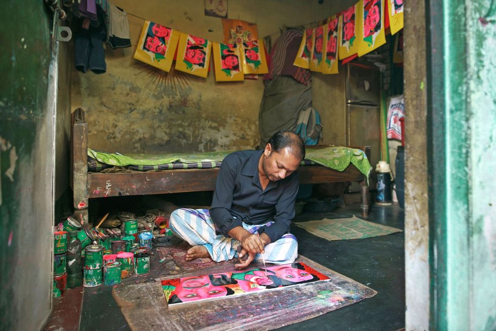Een man beschildert tinnen platen die worden gebruikt als decoratie op vaak zeer kleurrijke fietsriksjas
