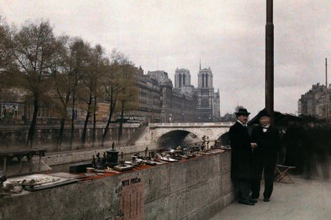 Twee mannen bieden snuisterijen te koop aan langs de oevers van de Seine in de jaren 20 van de vorige eeuw met de NotreDame op de achtergrond