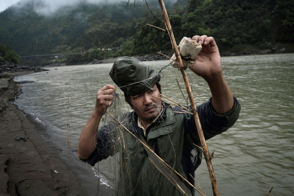 Li Zhen Xin een boer van dertig jaar oud maakt een net om vissen te vangen in Chala Veel boeren vissen in de rivier Nu om hun inkomen aan te vullen Dammen in de rivier zouden de migratie van vissen kunnen blokkeren