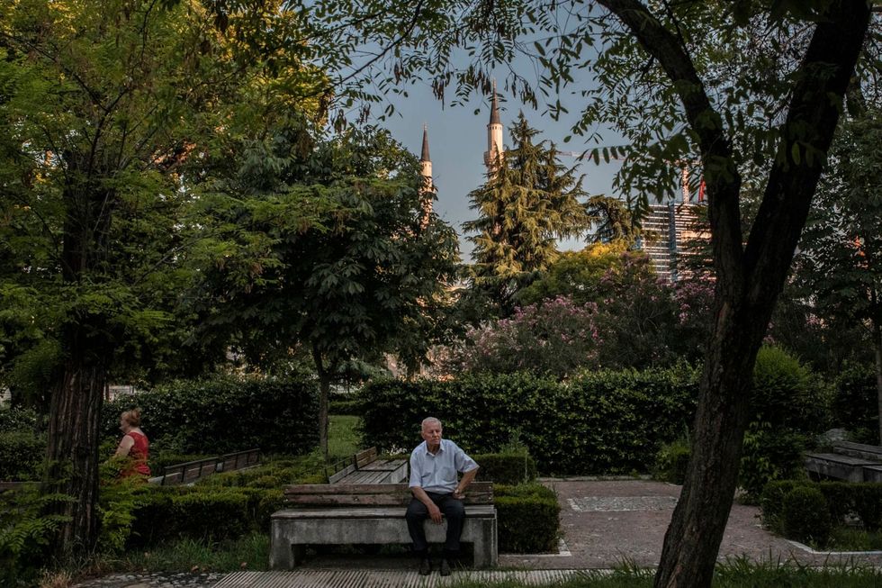 Tegen de achtergrond van de Namazgjamoskee zit een man in een park in het centrum van Tirana