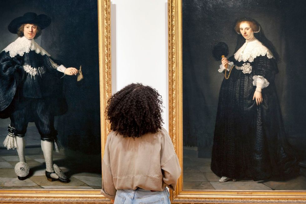 Een vrouw bekijkt twee museumstukken in het Rijksmuseum die licht werpen op de geschiedenis van de Nederlandse slavenhandel