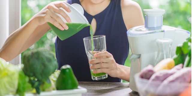 一個女生把打好的綠色果汁倒入玻璃杯
