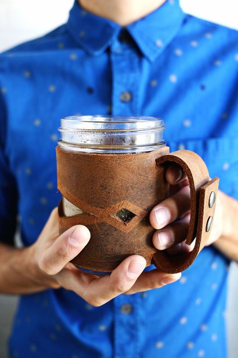 man holding a mason jar in a brown leather sleeve with handle