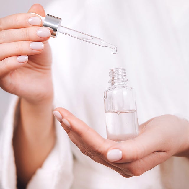 woman in bathrobe holding serum dropper into bottle