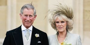 king charles iii, then prince charles, and camilla queen consort pictured on their wedding day, smiling and looking relaxed, outside the church charles is in a black suit and camilla in a grey coat dress with a feather headpiece