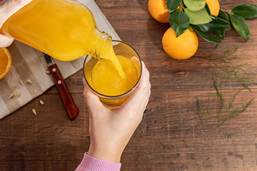 a hand of a person serving orange juice into a glass cup