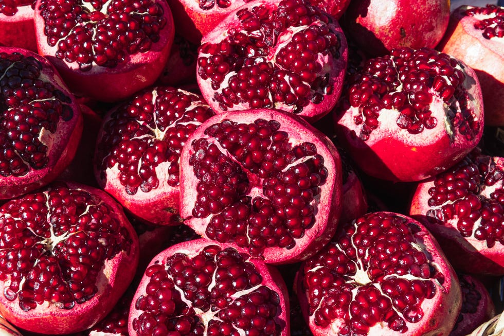 many ripe red pomegranates with top cut off, background close up