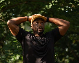 a person standing in a natural setting with arms raised and hands on head