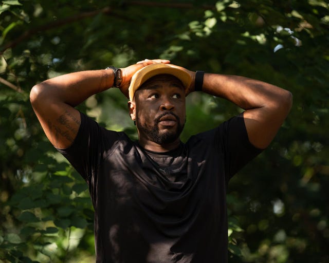 a person standing in a natural setting with arms raised and hands on head