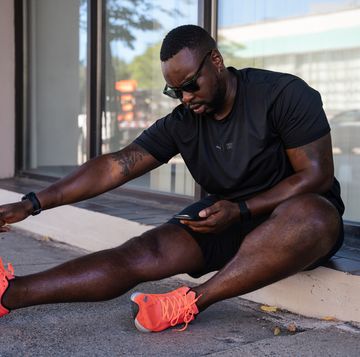 man stretching his hamstring after a run while looking at his phone