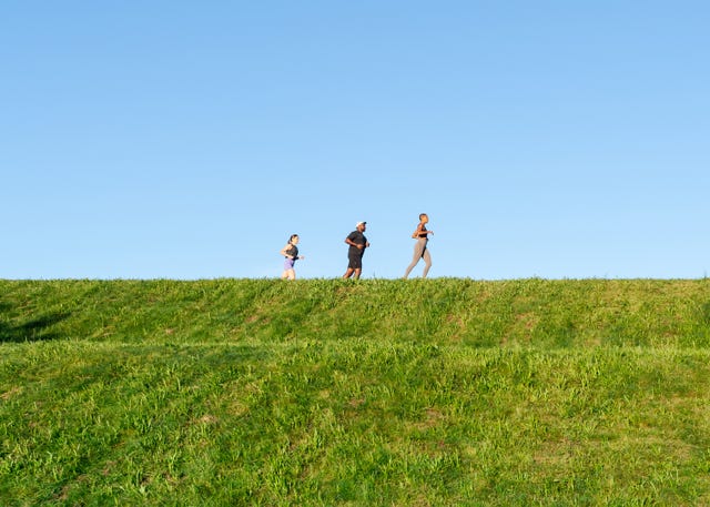 three people running along a ridge with a blue sky