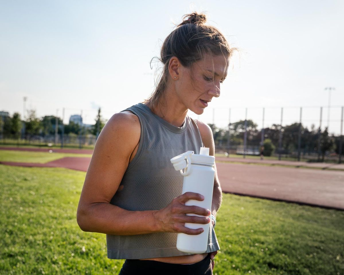 woman drinking water at the running track on a hot summer day