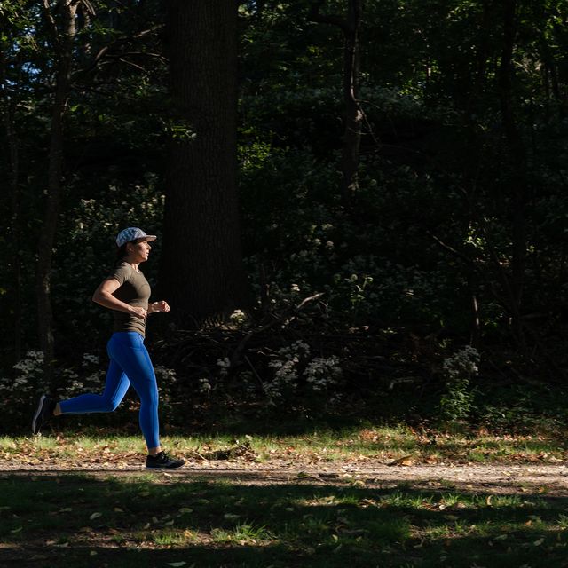 woman running along a trail with a background of dark trees